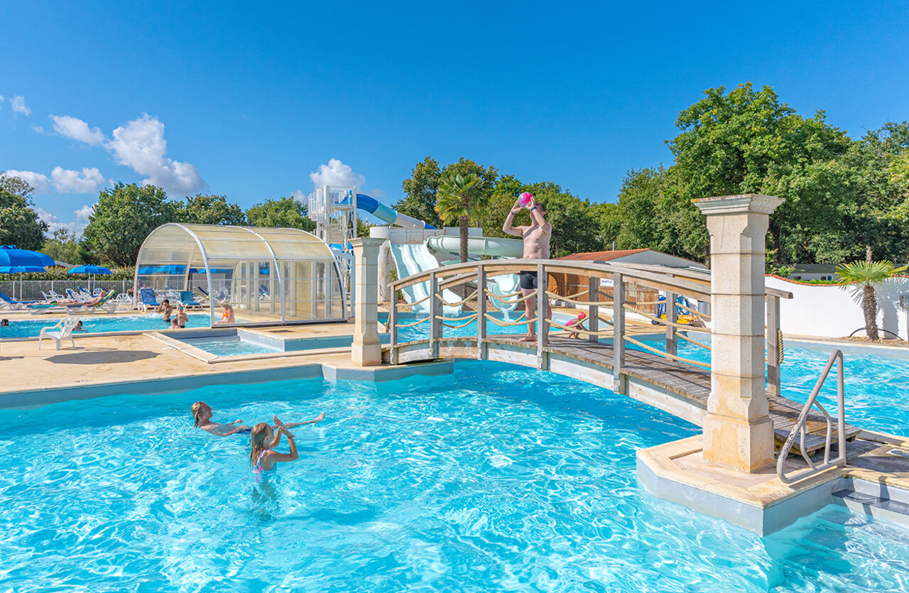 Piscina exterior, toboganes acu�ticos y puente decorativo en el camping VAGUES OCEANES Domaine les Charmilles en Saint-Laurent-de-la-Pr�e (17).