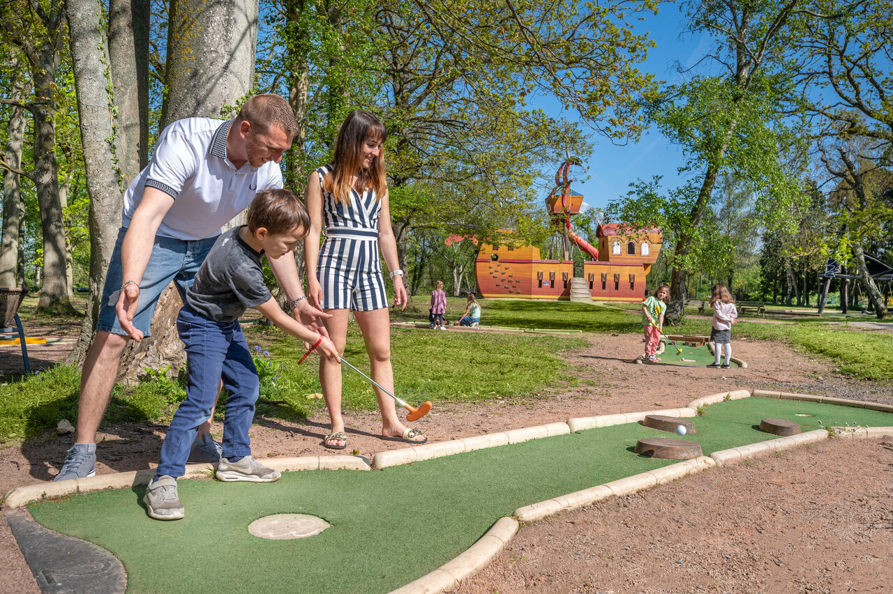 Familia jugando minigolf con zona de juegos en el camping CAPFUN Chateau d'Arvid en Villerville (14).