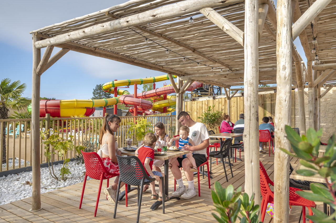 Familia almorzando en la terraza del restaurante con toboganes acu�ticos en el camping CAPFUN Chateau d'Arvid en Villerville (14).
