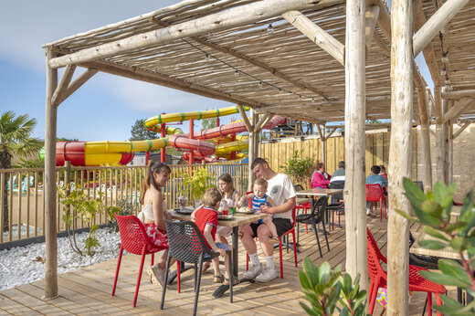 Familia almorzando en terraza del restaurante, toboganes acu�ticos en camping CAPFUN Chateau d'Arvid (14).