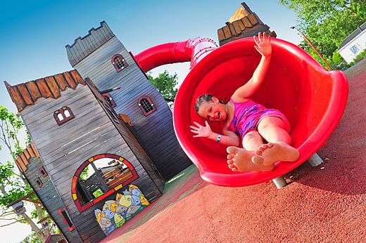 Niña feliz en tobogán rojo del parque infantil en camping CAPFUN Chênes en Medis/Royan (17).
