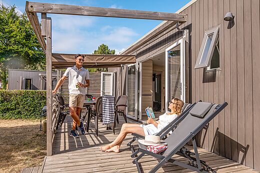 Mobil-home moderno con terraza de madera y pareja en el camping CLICOCHIC Chouans en SAINT HILAIRE DE RIEZ (85).