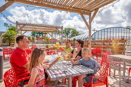 Familia con bebidas refrescantes en el bar exterior del camping CAPFUN Citadelle de Loustic.