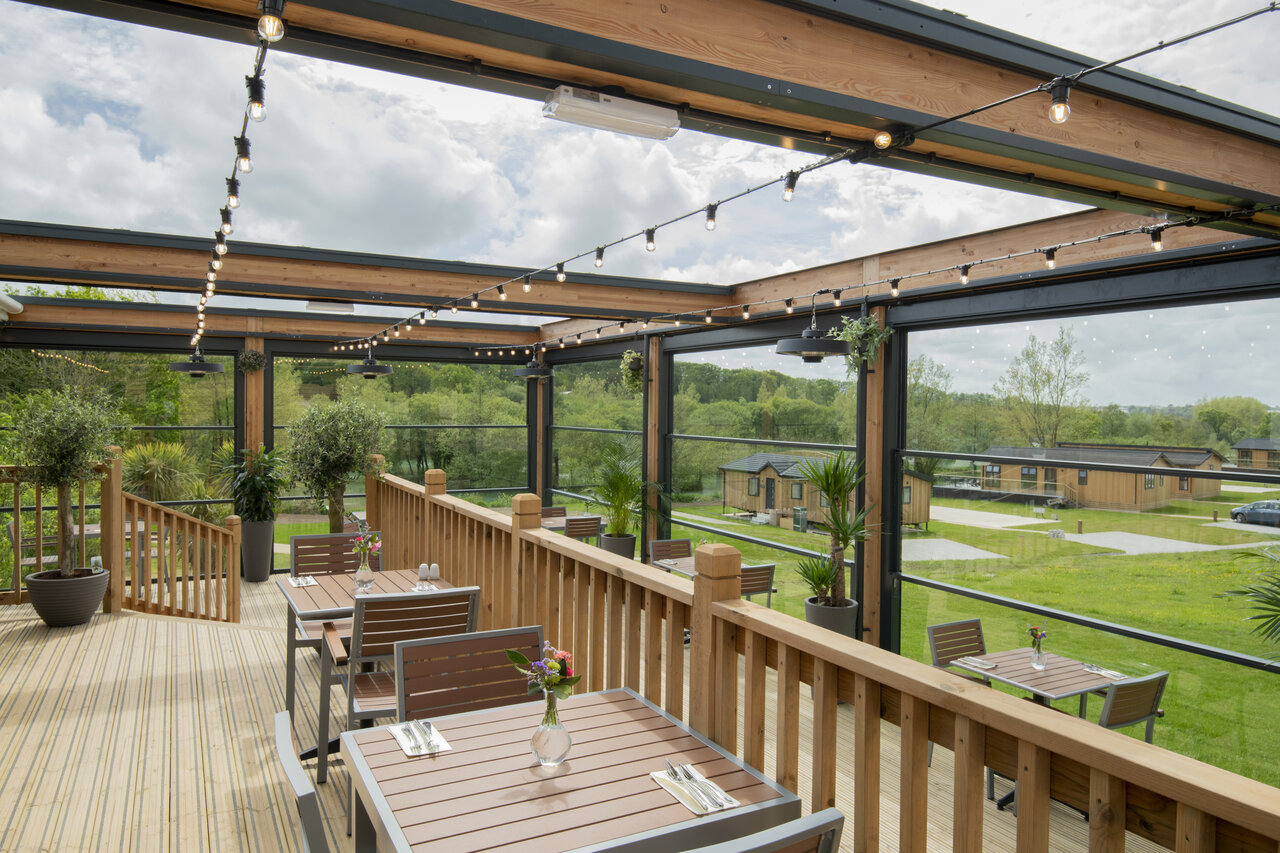 Terraza de restaurante exterior con mesas, vista a los lodges, CAPFUN UK Clawford Lakes.