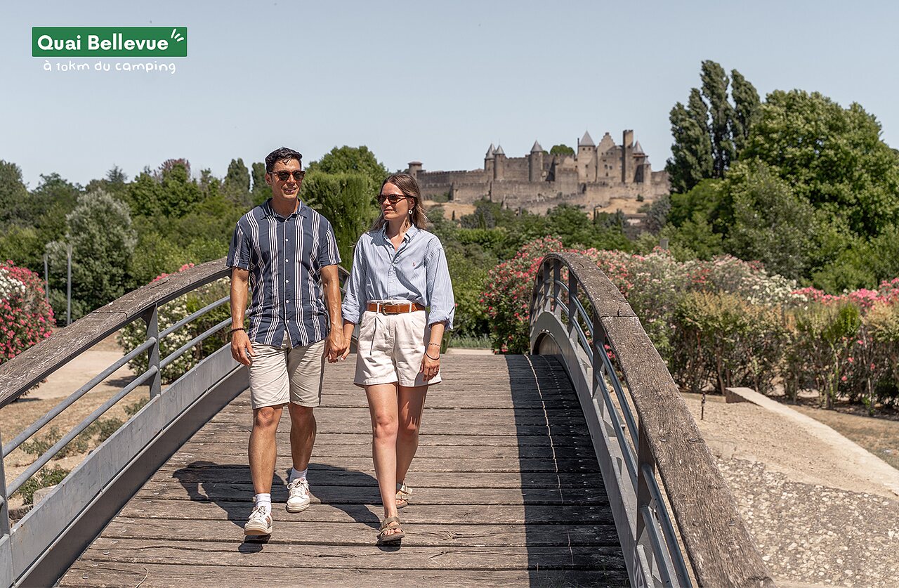 Pareja visitando la ciudad medieval de Carcasona desde un puente florido.