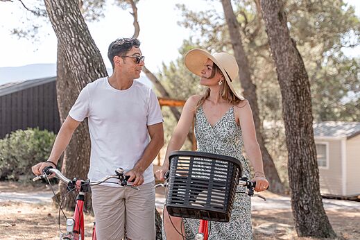 Pareja en bicicleta bajo los pinos en el camping CLICOCHIC Commanderie en Rustiques (11).