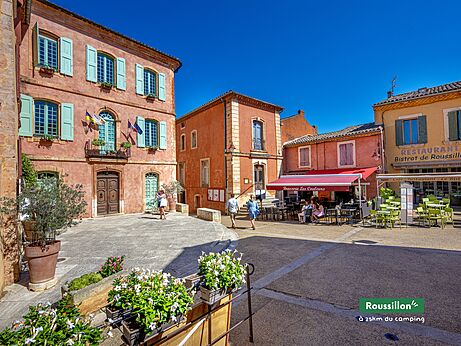 Plaza central del pueblo de Roussillon, casas coloridas y restaurante en Provenza.