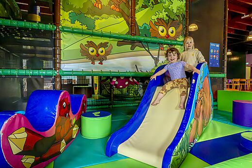 Niños sonrientes en un tobogán del parque infantil cubierto en el camping CAPFUN De Belten en Rheeze.