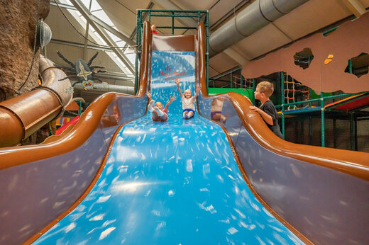 Tobogán gigante interior con niños sonrientes en el camping CAPFUN De Bongerd en Tuitjenhorn.