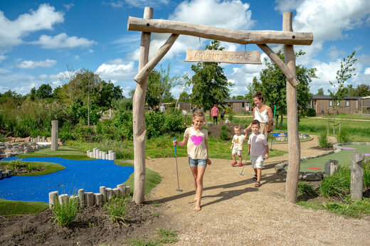 Familia jugando al minigolf de aventura bajo el arco de madera en el camping CAPFUN De Bongerd en Tuitjenhorn.