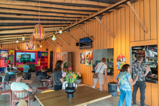 Zona de restaurante colorida con mostrador de servicio y mesas en el camping CAPFUN De Bongerd a Tuitjenhorn.