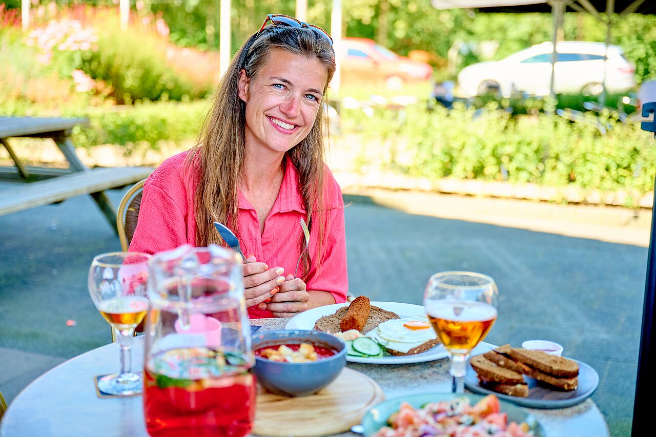 Mujer sonriente almorzando en terraza del camping CAPFUN De Eikenhof en Paasloo/Oldemarkt.