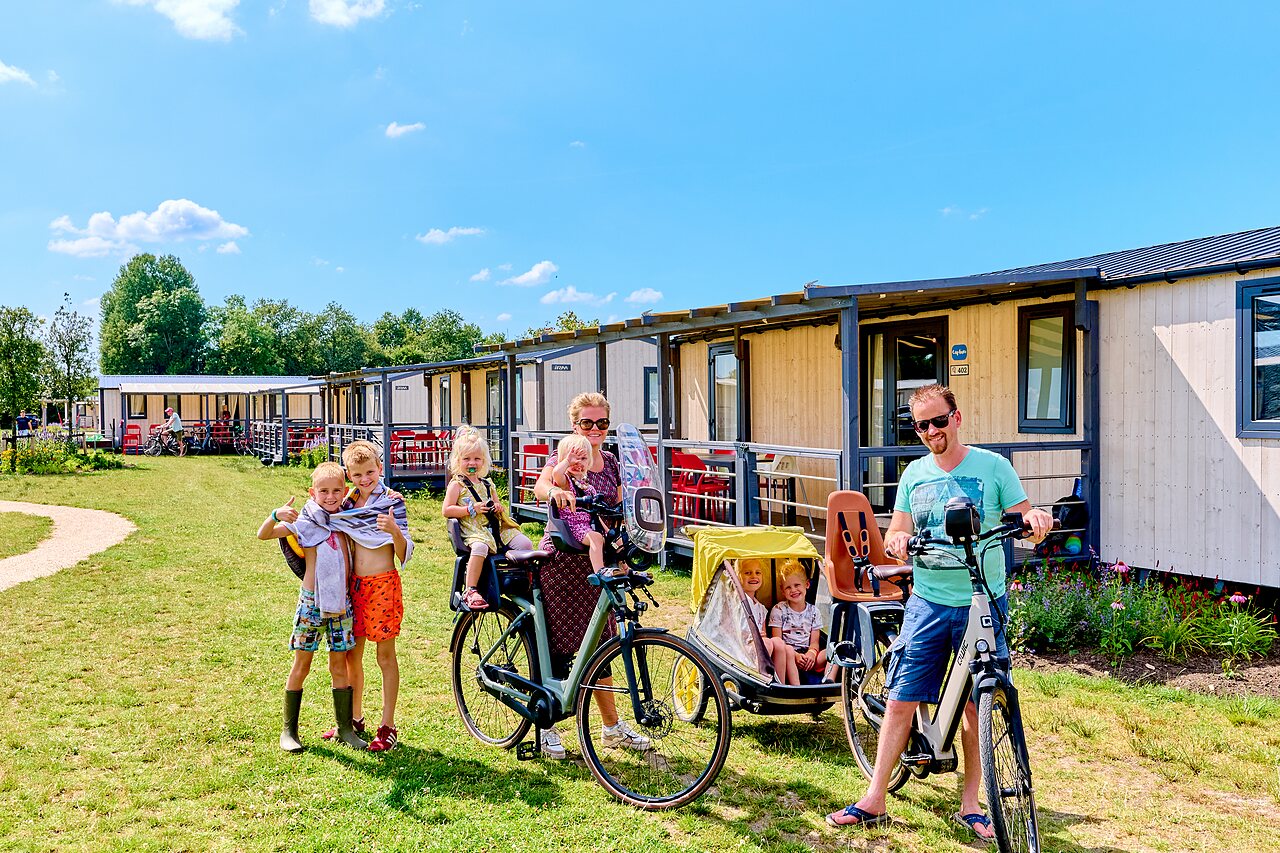 Familia en bicicleta frente a mobil-homes modernos en CAPFUN De Eikenhof en Paasloo/Oldemarkt.