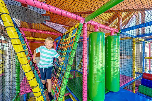 Niño sonriente en una estructura de juegos interior colorida en el camping CAPFUN De Eikenhof en Paasloo/Oldemarkt.