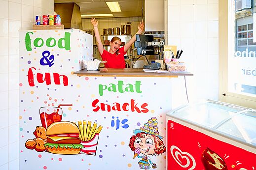 Joven sonriente detrás del mostrador del snack-bar "Food & Fun" en el camping CAPFUN De Eikenhof en Paasloo/Oldemarkt.