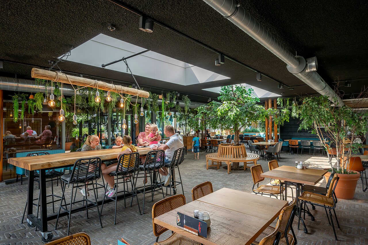 Restaurante moderno con familias y decoraci�n vegetal en el camping CAPFUN De Pekelinge en Oostkapelle.