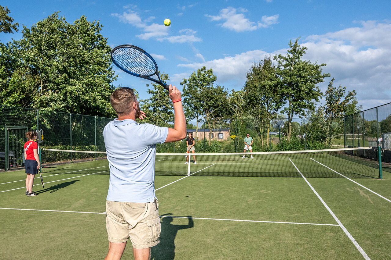 Jugadores de tenis en una cancha exterior soleada en el camping CAPFUN De Pekelinge en Oostkapelle.