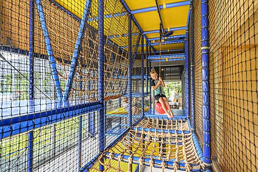 Niño sonriente jugando en estructura de juegos interior en camping CAPFUN De Pekelinge en Oostkapelle.