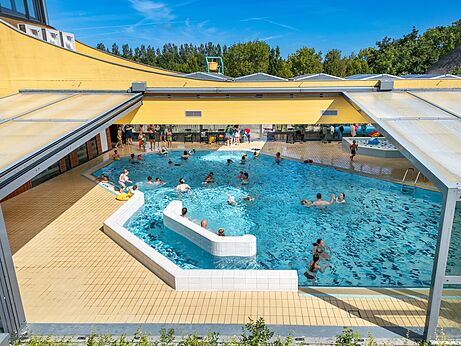 Gran piscina exterior e interior con bañistas en el camping CAPFUN De Pekelinge en Oostkapelle.