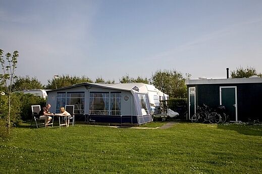 Caravana con toldo y parcela verde en el camping CAPFUN De Pekelinge en Oostkapelle.
