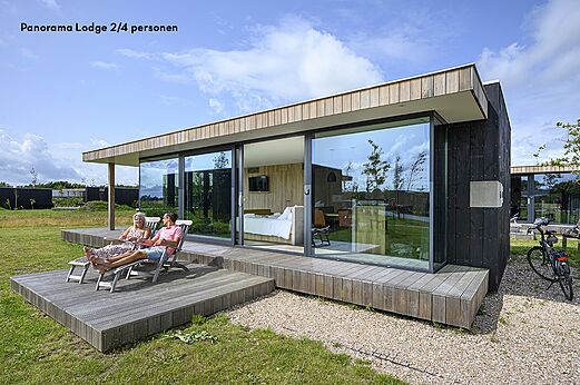Lodge moderno con terraza y pareja relajándose en el camping CAPFUN De Pekelinge en Oostkapelle.