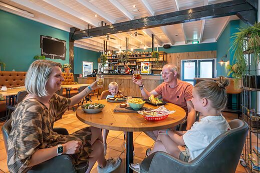 Familia sonriente cenando en el restaurante del camping CAPFUN De Pekelinge en Oostkapelle.