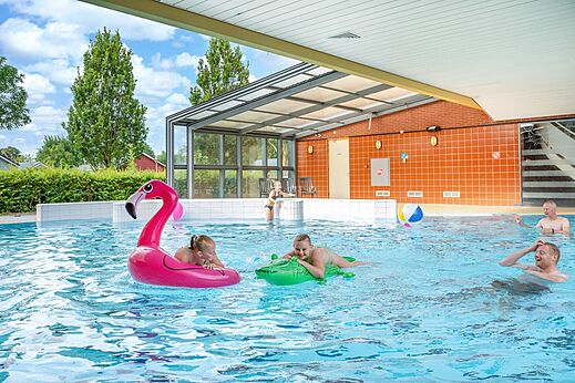 Piscina cubierta y exterior con familia y flotadores en el camping CAPFUN De Pekelinge en Oostkapelle.