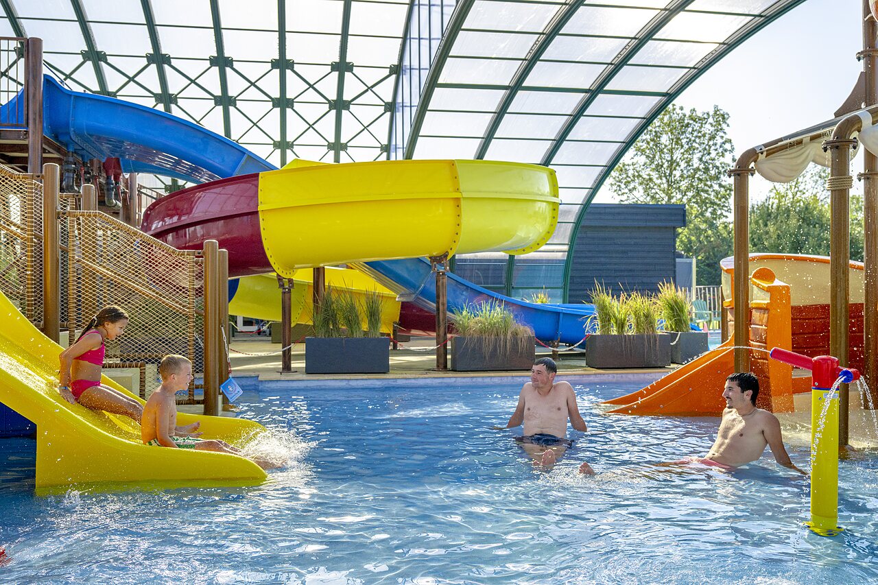 Toboganes acu�ticos coloridos y piscina cubierta con ni�os y adultos en el camping CAPFUN De Rotonde en Enspijk.