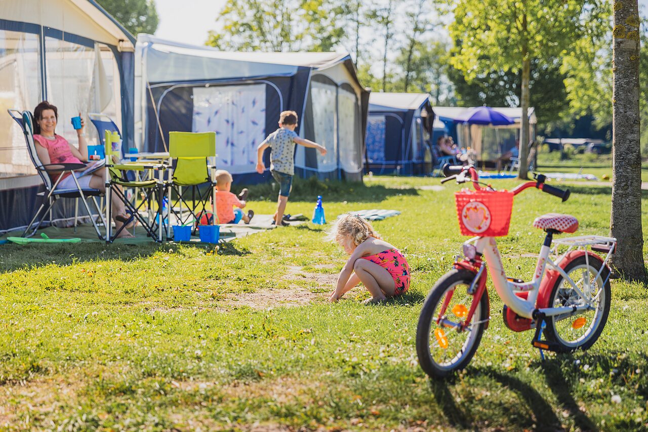Parcela de camping familiar con ni�os jugando y bicicleta en CAPFUN De Rotonde en Enspijk.