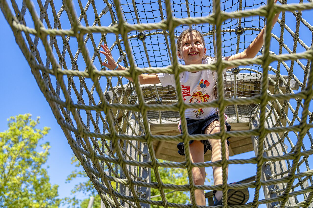 Ni�a sonriente escalando estructura de juegos de cuerda en el camping CAPFUN De Rotonde en Enspijk.