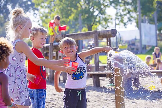 Niños felices jugando con agua y vasos en el área de juegos del camping CAPFUN De Rotonde en Enspijk.