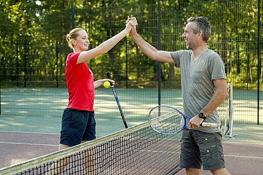Cancha de tenis con jugadores sonrientes en el camping CAPFUN De Scheepsbel.