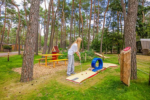 Mujer jugando al minigolf en un entorno boscoso en el camping CAPFUN De Scheepsbel en Doornspijk.