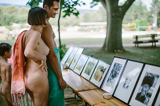 Familia naturista viendo exposición de fotos en camping LIBRANOO Naturiste Belezy, Bédoin.