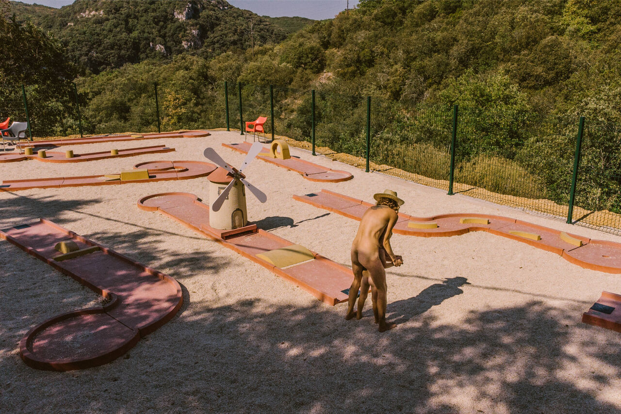 Campo de minigolf con molino, persona naturista jugando en el camping LIBRANOO Naturiste Sabliere en Barjac (30).