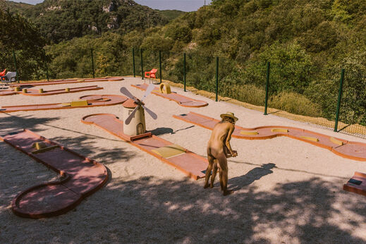 Campo de minigolf con molino, persona jugando en el camping LIBRANOO Naturiste Sabliere.