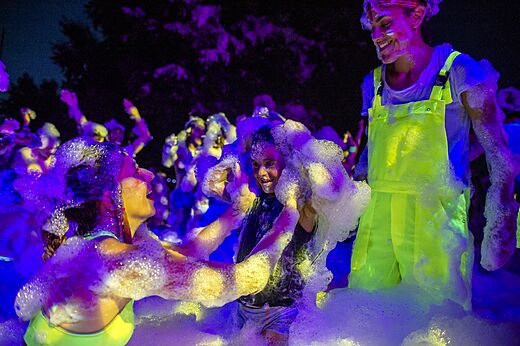 Fiesta de la espuma nocturna con participantes sonrientes y luces UV en el camping CAPFUN Donjon de Lars en Courseulles-sur-Mer (14).