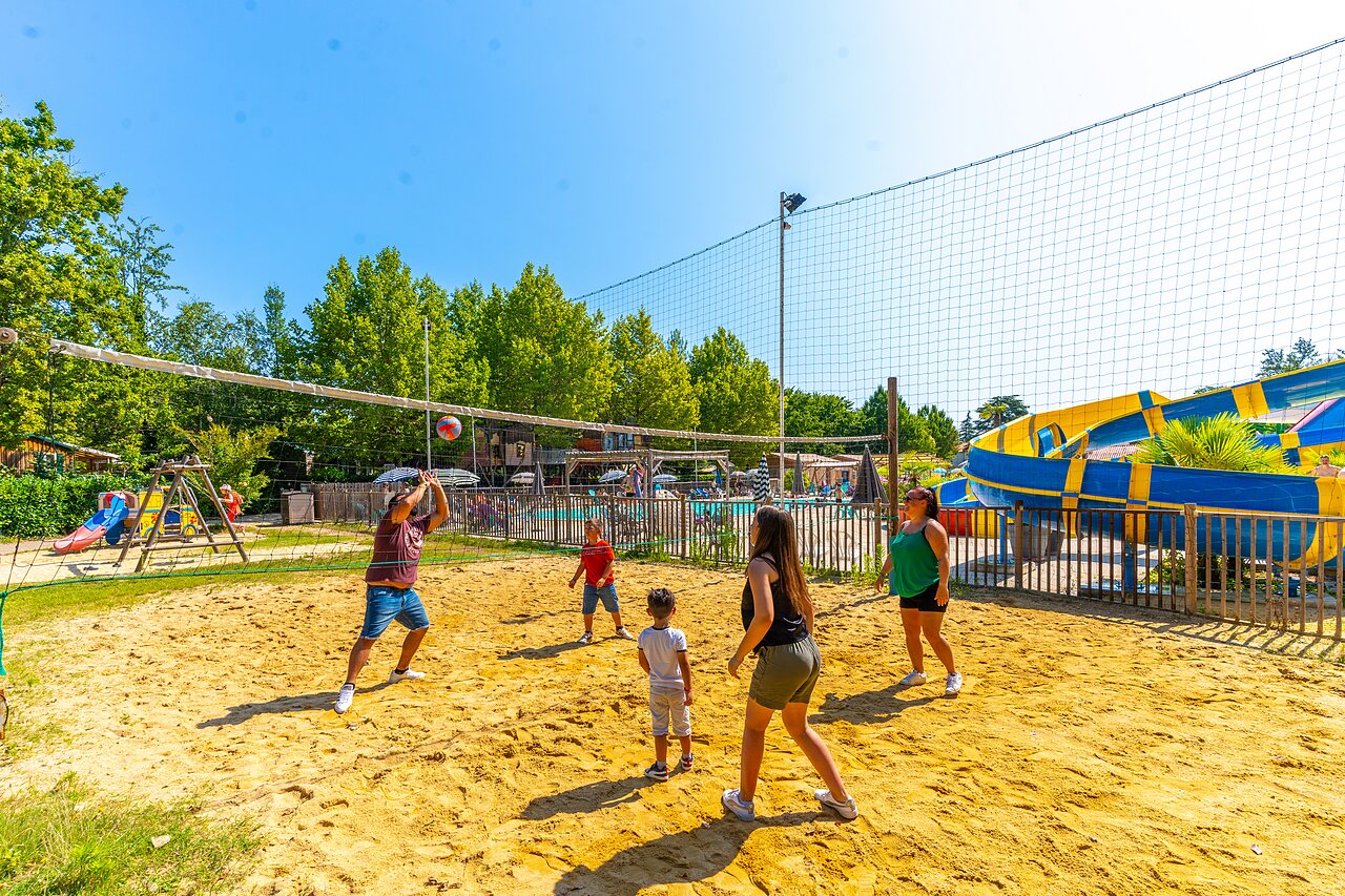 Familia jugando voleibol de playa en cancha de arena, toboganes acu�ticos en camping CAPFUN Duravel.