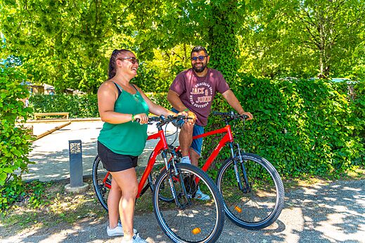 Pareja sonriente con bicicletas rojas en el camping CAPFUN Duravel en Duravel (46).
