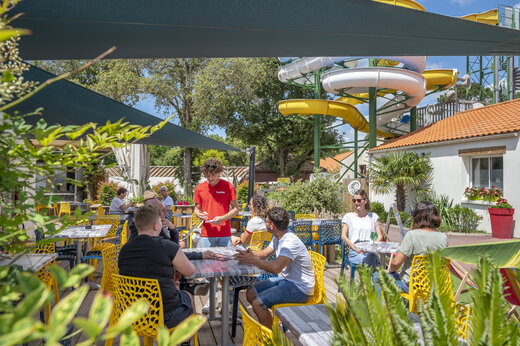 Terraza de restaurante animada con clientes y camarero en el camping CAPFUN Ecureuils en JARD SUR MER (85).