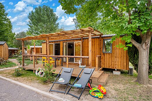 Mobil-home de madera con terraza cubierta y sillas en el camping CAPFUN El Moli en Elne (66).