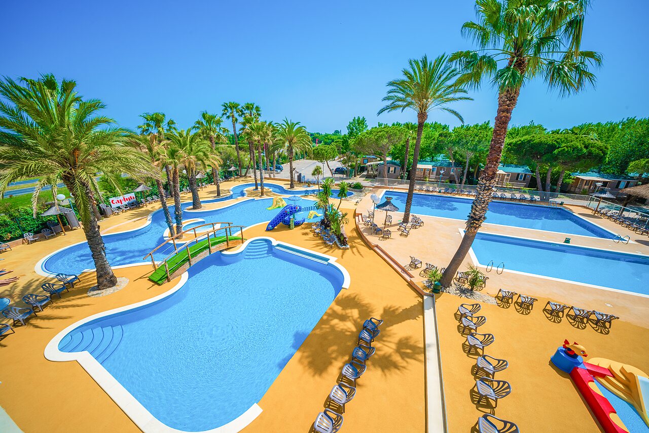 Piscinas exteriores, toboganes y palmeras del camping CAPFUN Emeraude en Portiragnes (34).