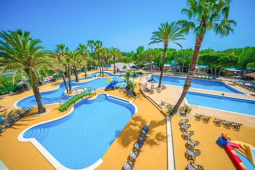 Gran piscina exterior con toboganes y palmeras en el camping CAPFUN Emeraude en Portiragnes (34).