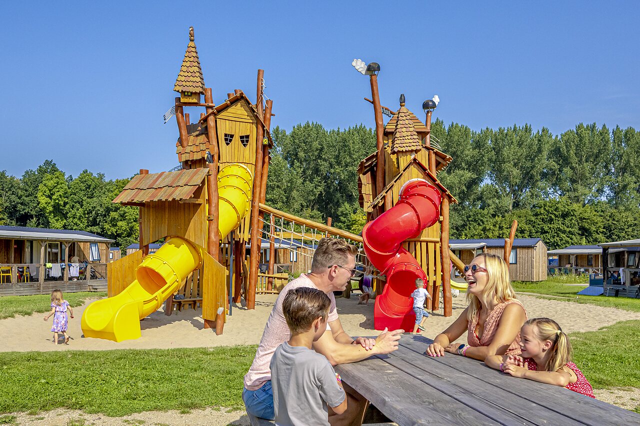 Zona de juegos con toboganes y familia feliz en el camping CAPFUN Erkemederstrand, Zeewolde.