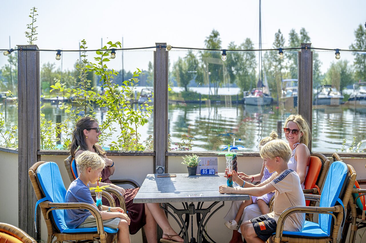Familia en el bar, bebidas refrescantes, vista al lago en el camping CAPFUN Erkemederstrand en Zeewolde.