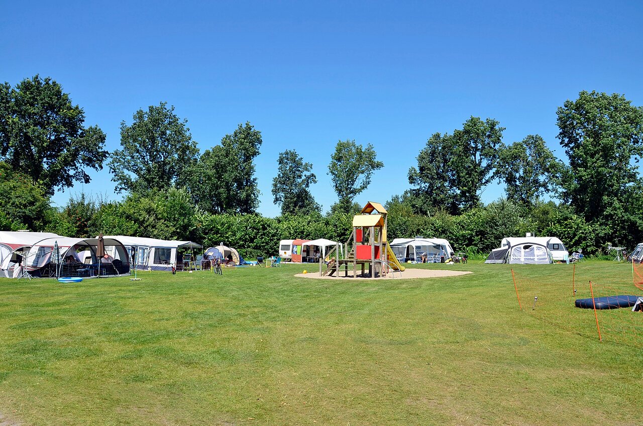 Parcelas de camping verdes con zona de juegos y caravanas en el camping CAPFUN Erkemederstrand en Zeewolde.