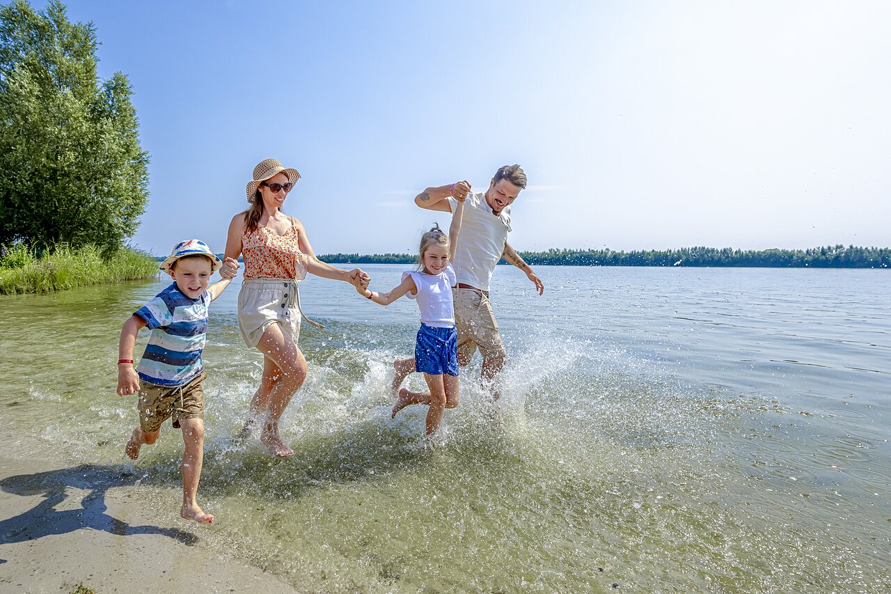 Familia feliz corriendo y salpicando en el agua poco profunda en el camping CAPFUN Erkemederstrand en Zeewolde.