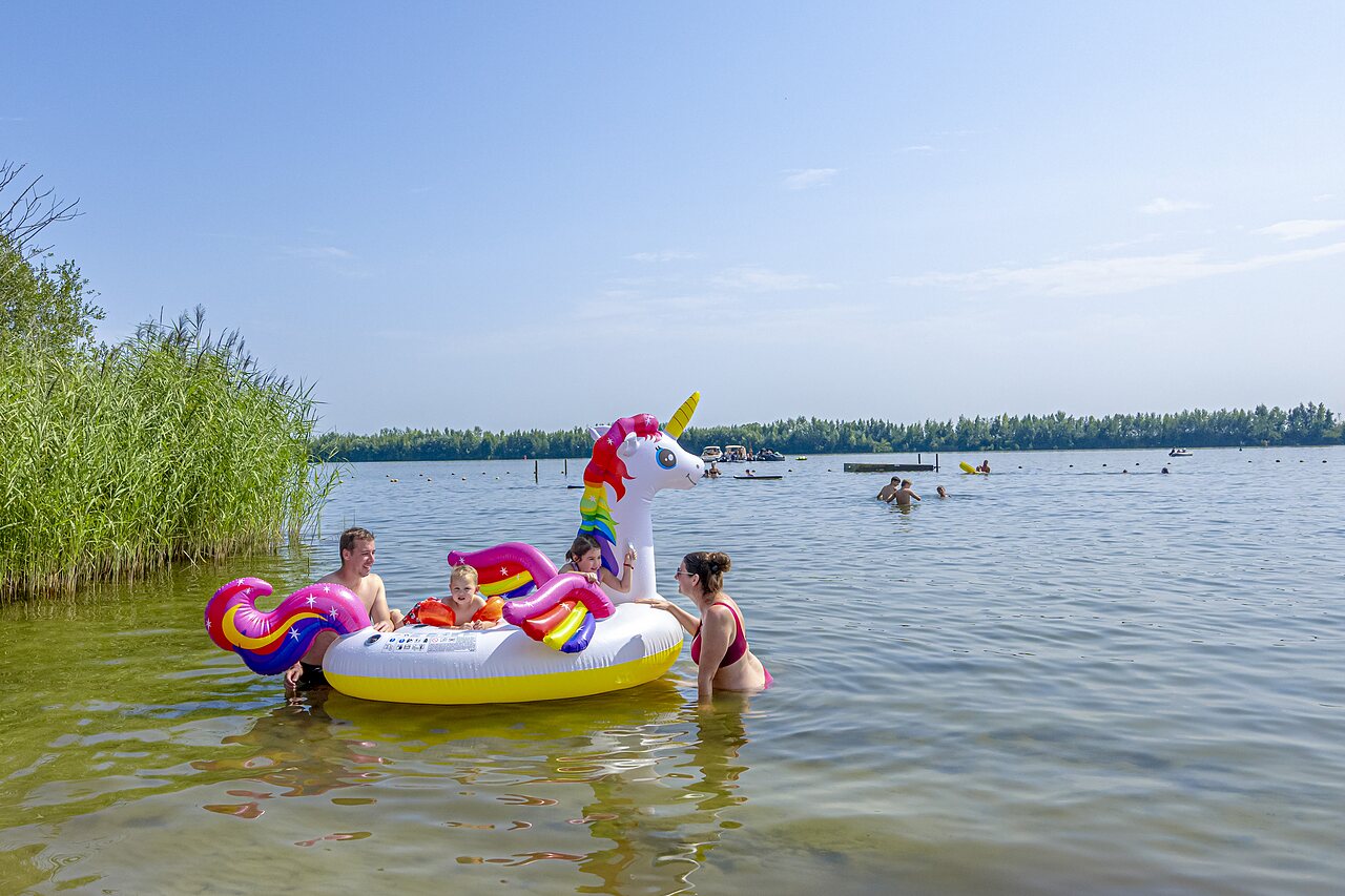 Familia jugando en el lago con unicornio inflable en el camping CAPFUN Erkemederstrand en Zeewolde.