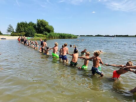 Niños jugando al tira y afloja en el agua, camping CAPFUN Erkemederstrand en Zeewolde.