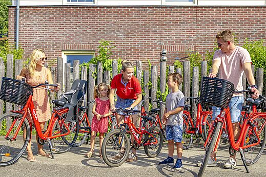 Familia alquilando bicicletas rojas con asiento infantil en el camping CAPFUN Erkemederstrand en Zeewolde.